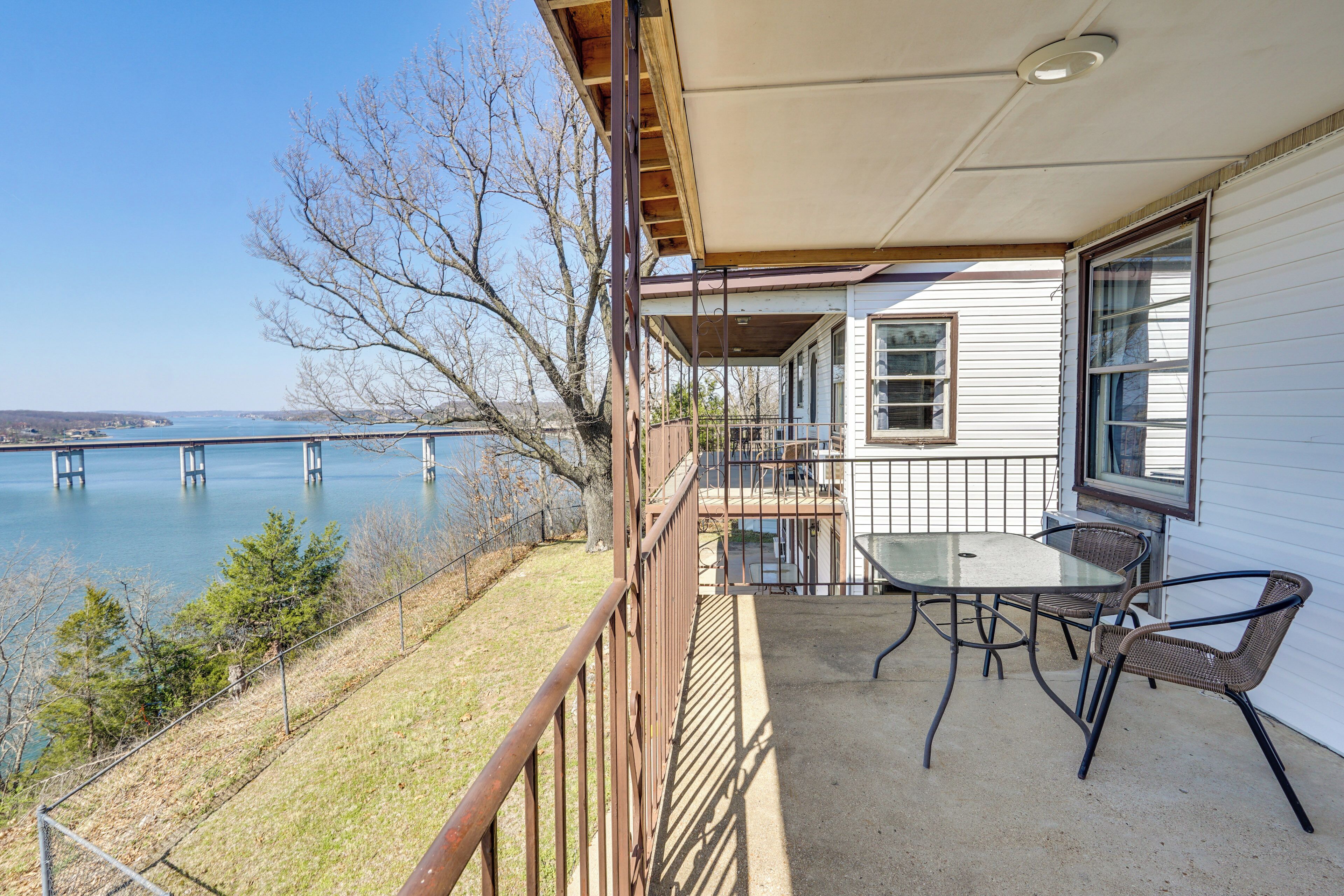 A balcony with a table and chairs, overlooking a body of water and a bridge.