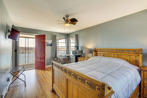 A bedroom with a wooden bed, a ceiling fan, a TV, a desk, and a balcony door. - Unit 2: Pool, Lake & View! Studio By Bagnell Strip (Lake Ozark)
