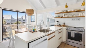 A modern kitchen with white cabinetry, a built-in oven, and a large window overlooking a balcony. - Your seat for sweeping ocean views and unforgettable sunsets at Villa 22 (Bald Head Island)