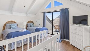 A bedroom with two beds, a TV, a white dresser, and a balcony with a view. - Your seat for sweeping ocean views and unforgettable sunsets at Villa 22 (Bald Head Island)