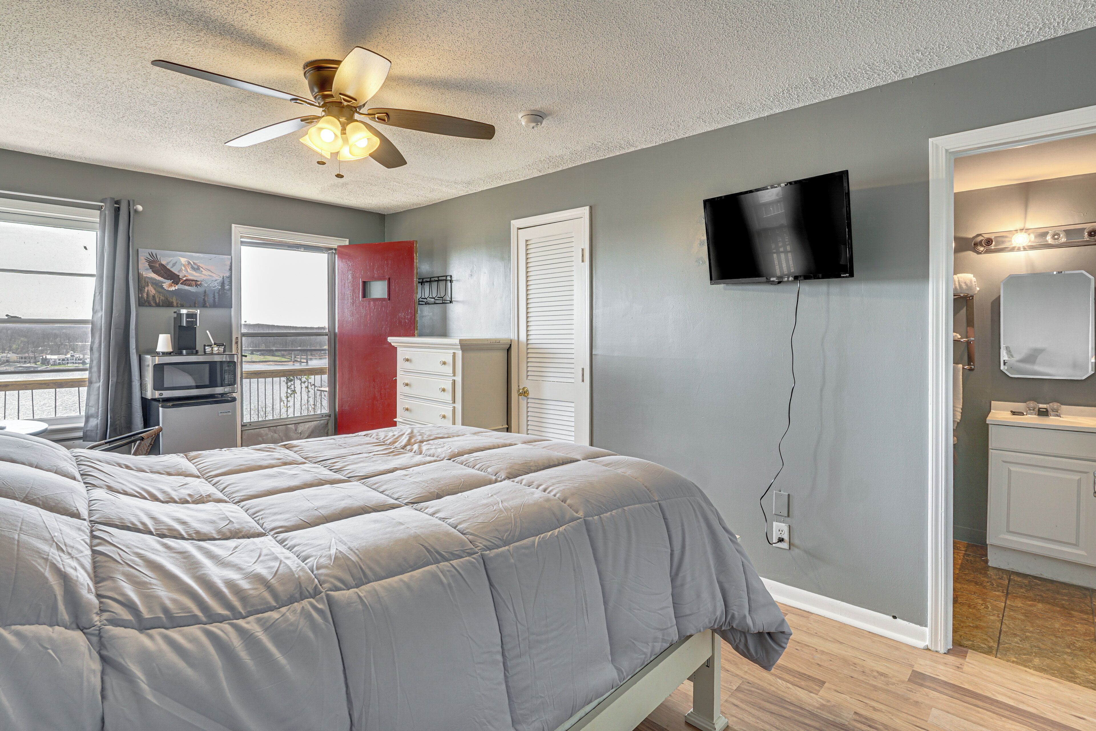 A bedroom with a bed, a ceiling fan, a TV, and a bathroom with a mirror.
