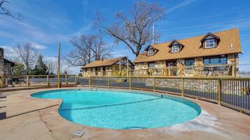 A swimming pool with a stone deck, surrounded by a wooden fence, and a building with a stone facade and multiple windows in the background.