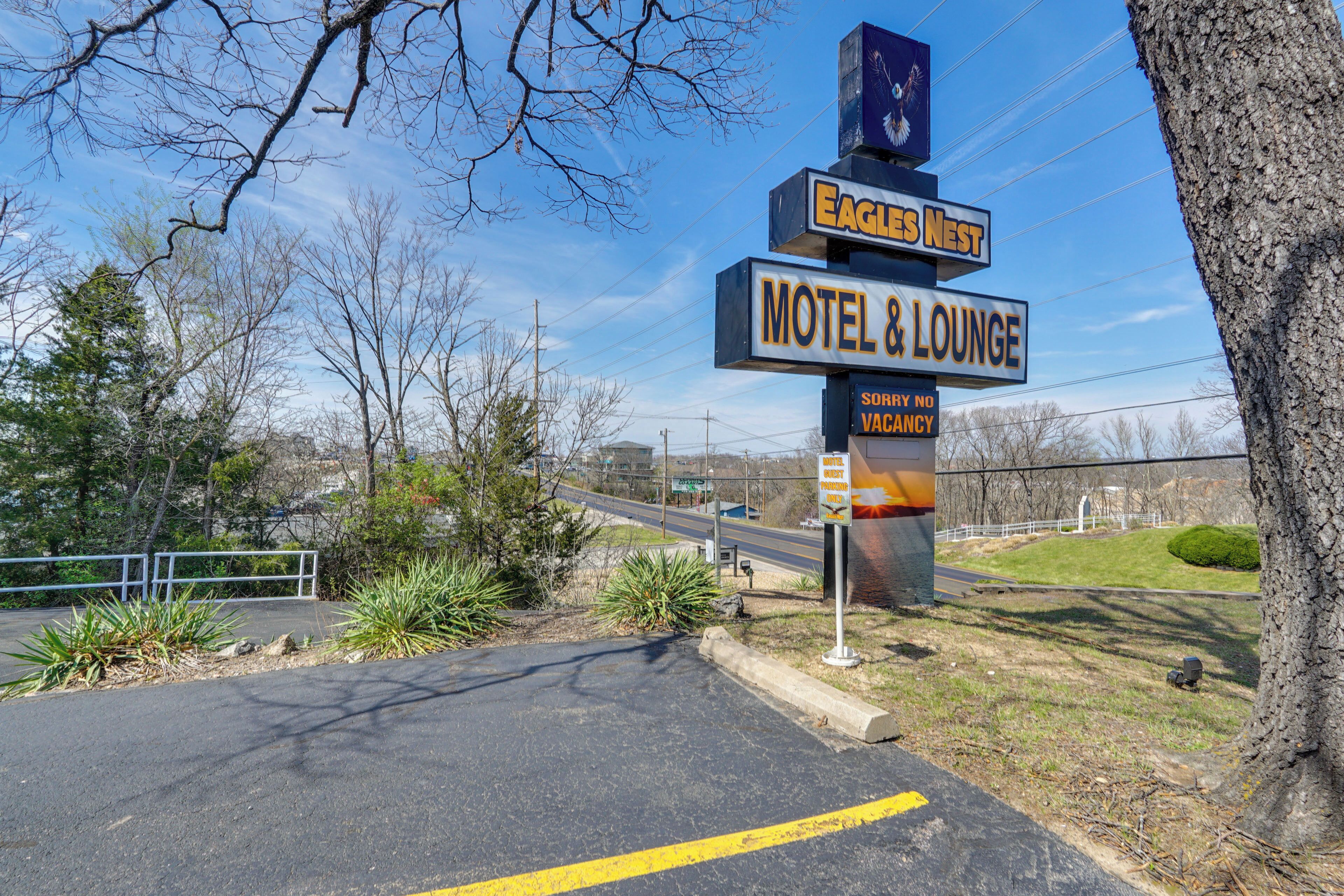 A motel sign with 'Eagles Nest' and 'Motel & Lounge' text, a parking lot, and a road in the background.