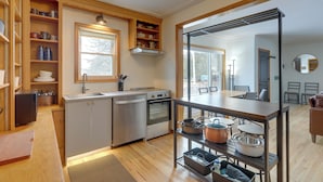 A compact kitchen with built-in appliances, wooden shelves, and a dining area with a view. - Lake Access Home on Cross Lake: Walk to Dtwn! (Pine City)