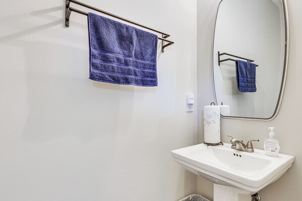 A bathroom with a white sink, a mirror, a towel rack with a blue towel, and toiletries. - Traveling Professionals Welcome! Cozy Athens Home (Athens)
