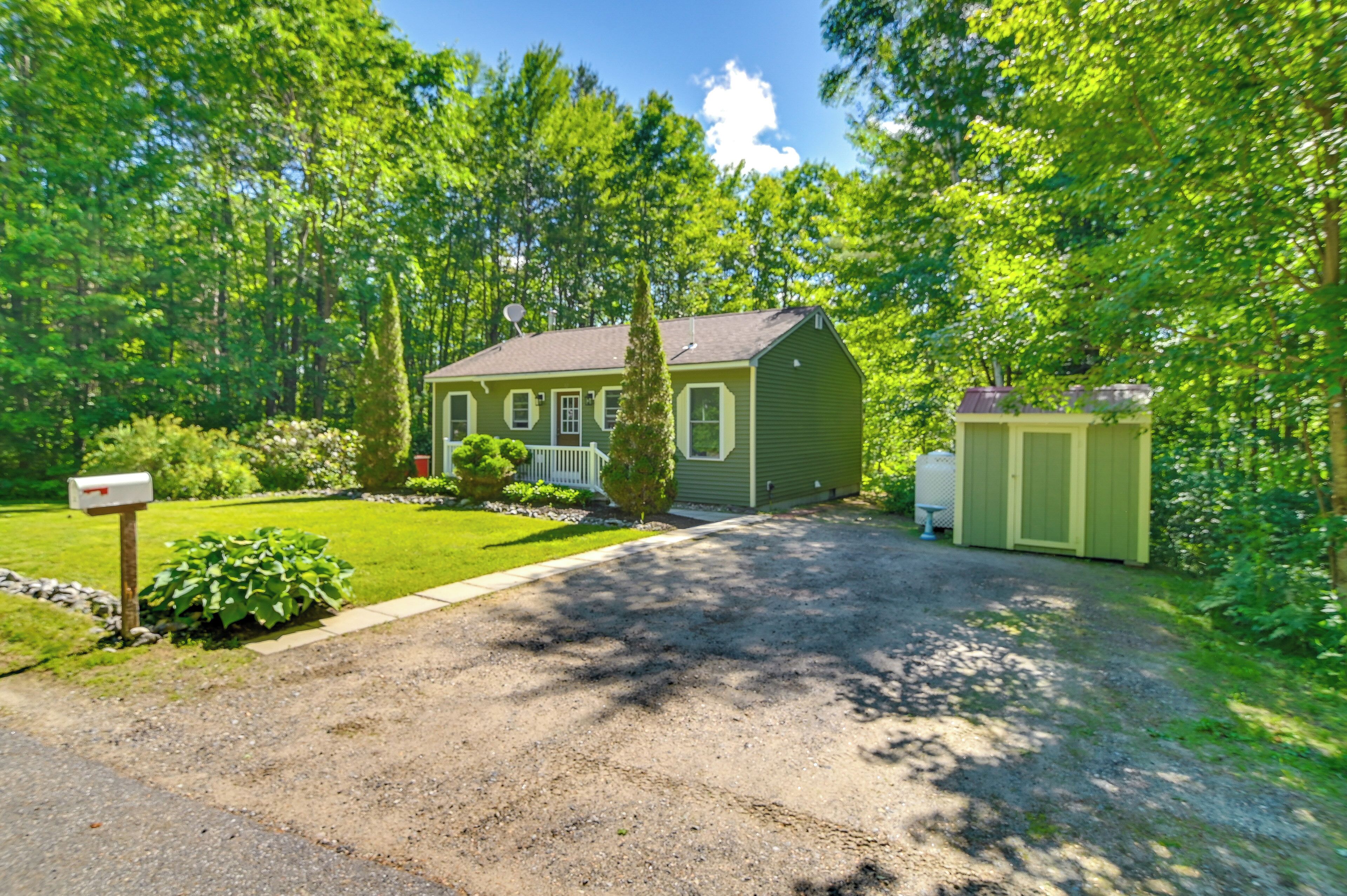 A green house with a gravel driveway, surrounded by lush greenery and trees.