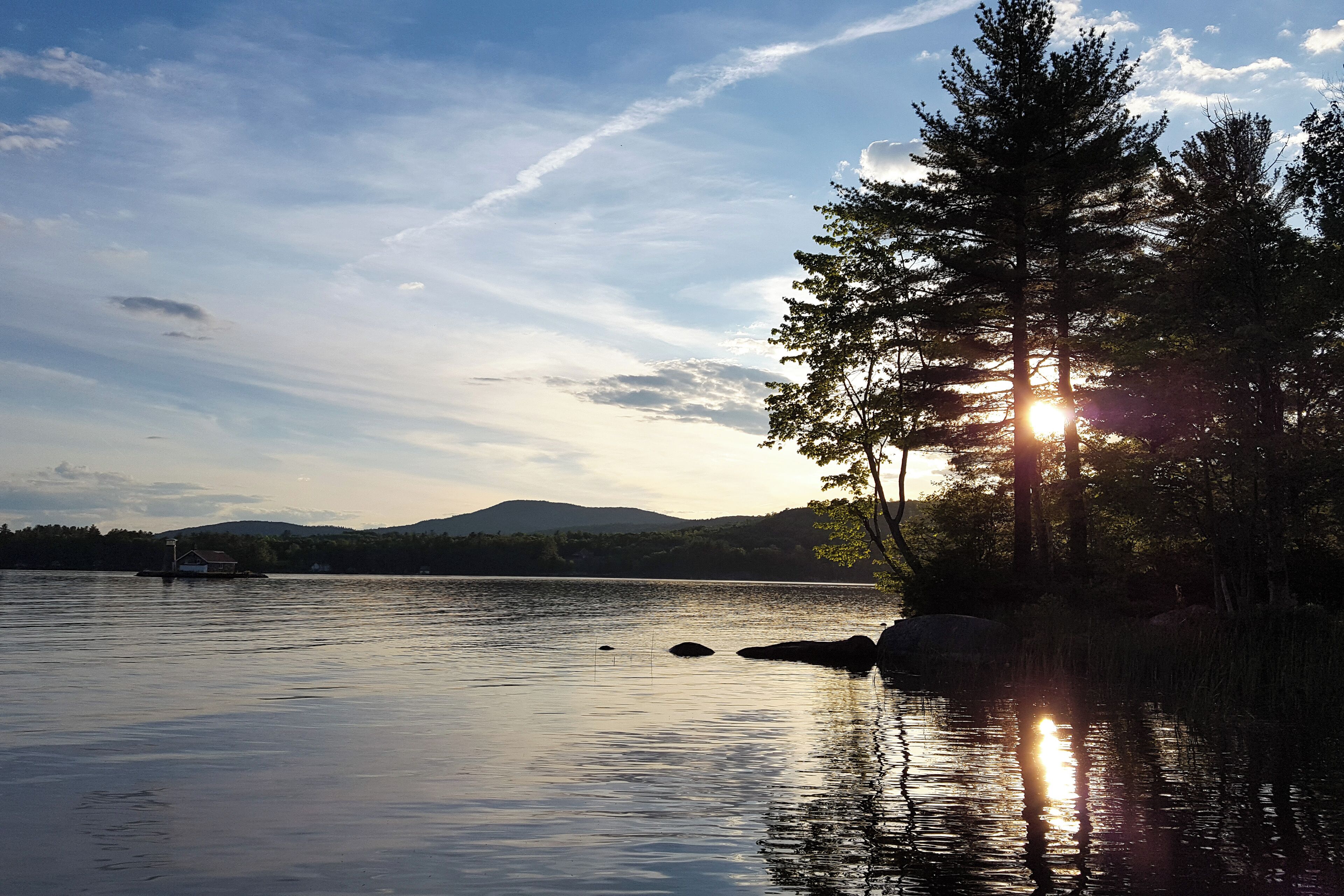 Un lac paisible, bordé d’arbres, avec une chaîne de montagnes qui se dessine à l’horizon.