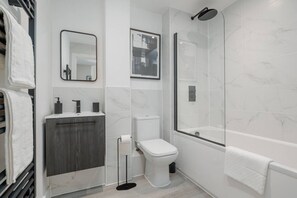 Un baño moderno con inodoro, lavabo, espejo y ducha.