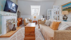 Ein Wohnzimmer mit Fernseher, Korbmöbeln, Kamin und Bücherregal.