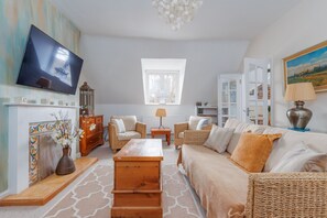 Ein Wohnzimmer mit Fernseher, Korbmöbeln, Kamin und Bücherregal.