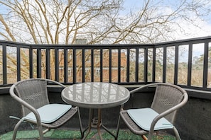 Ein Balkon mit zwei Korbstühlen und einem runden Tisch, mit Blick auf ein Backsteingebäude und kahl stehende Bäume.