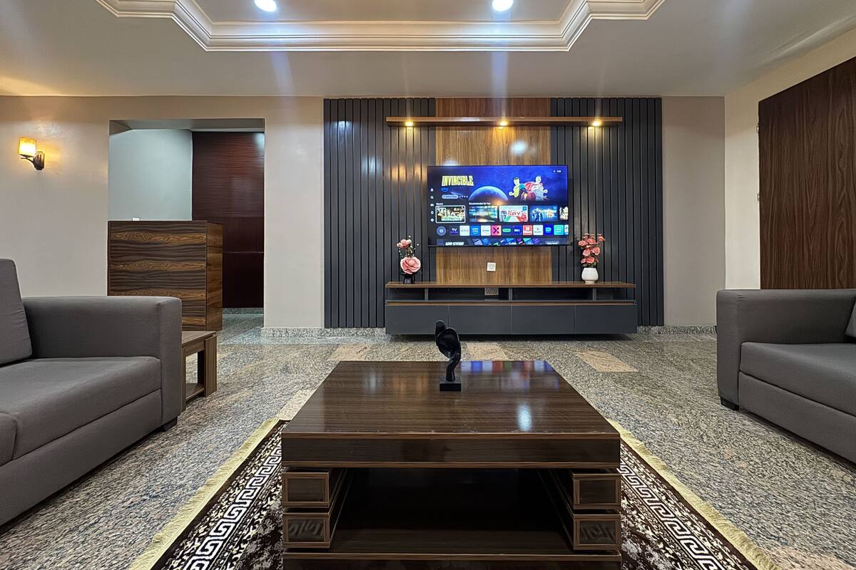 A modern living room with a flat-screen TV, two sofas, a coffee table, and a patterned rug.