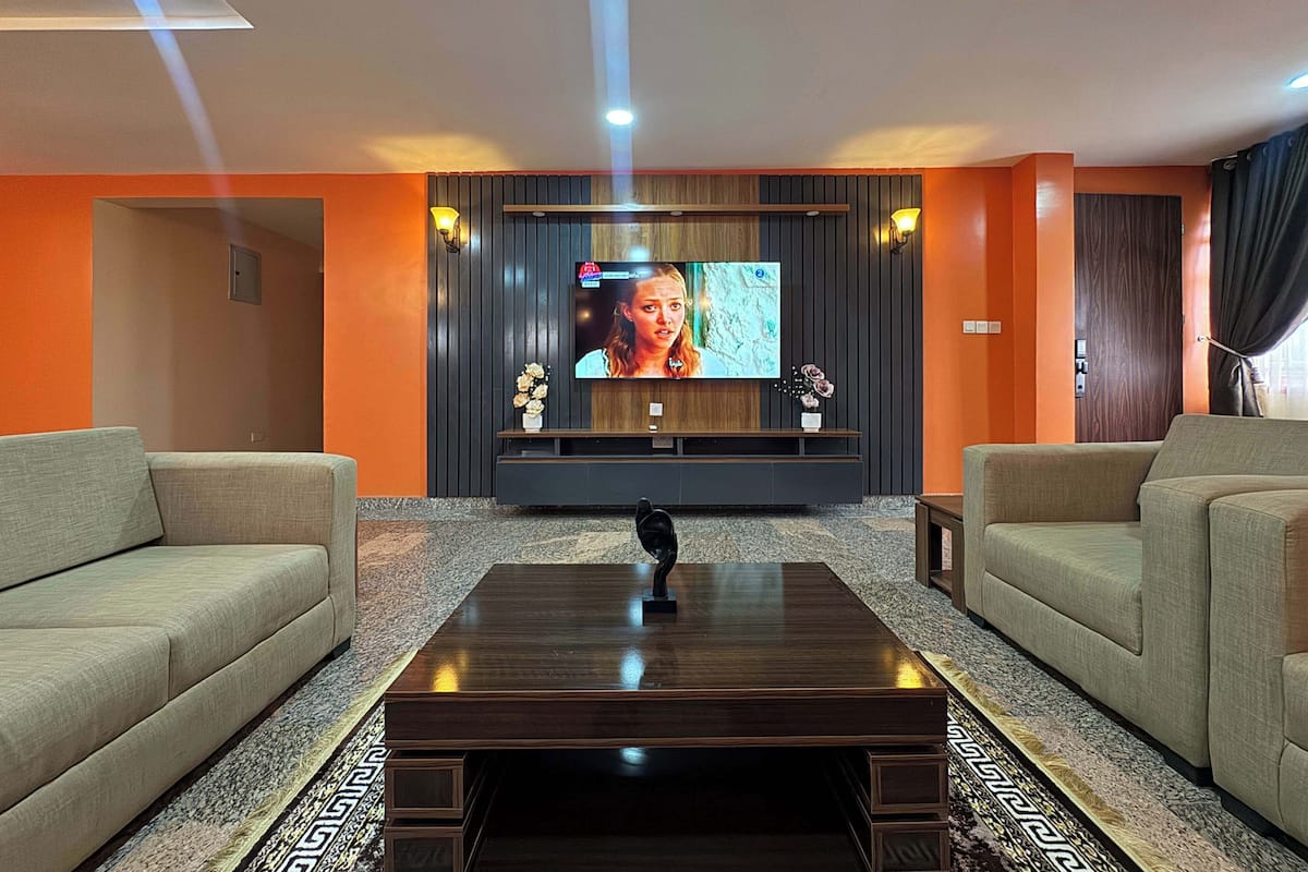 A modern living room with a flat-screen TV, sofas, a coffee table, and a decorative vase.