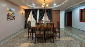 Un coin repas avec une table et des chaises, un lustre, un tableau au mur et une porte à l’arrière-plan.