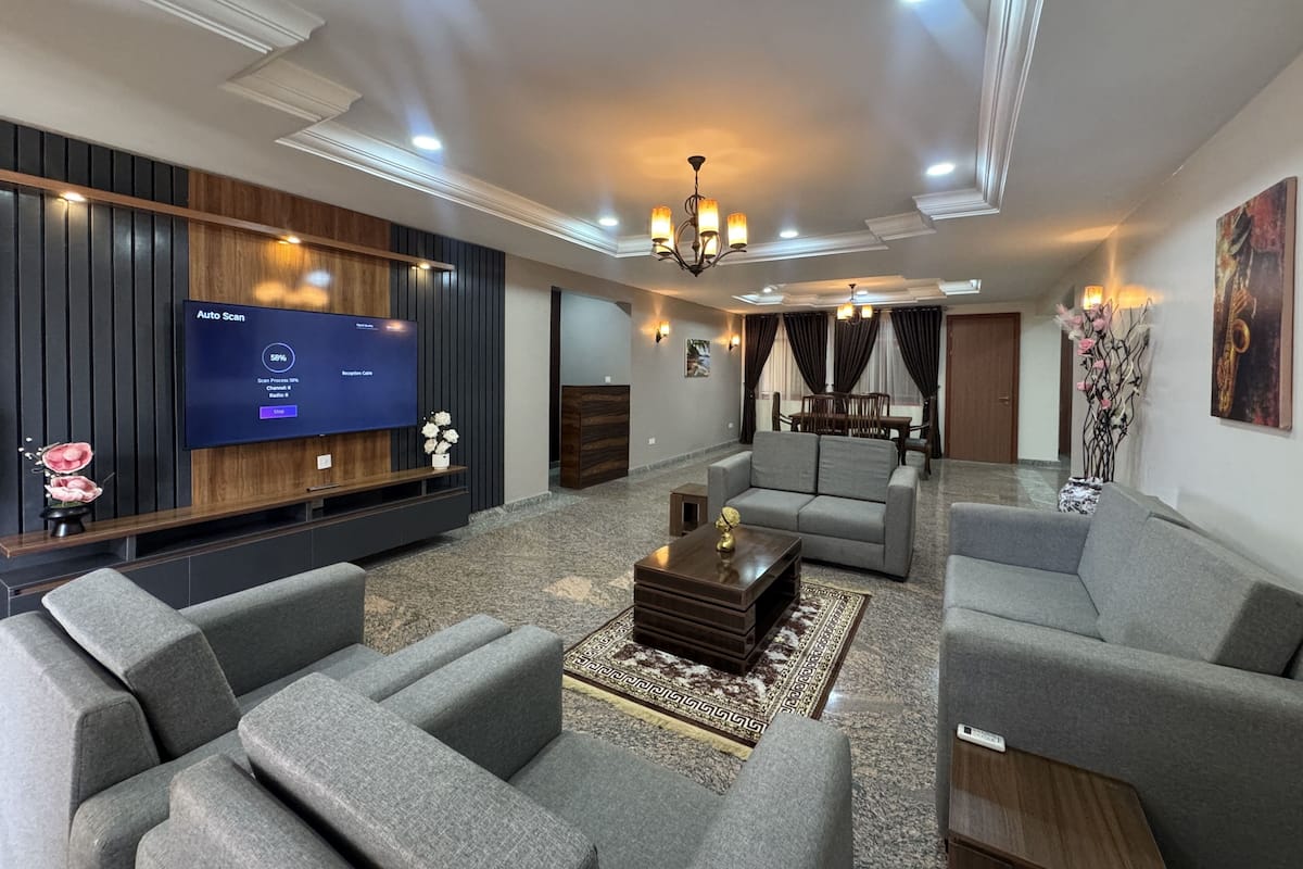 A modern living room with a flat-screen TV, sofas, a coffee table, and a chandelier.