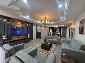 A modern living room with a flat-screen TV, sofas, a coffee table, and a chandelier. - R & R Apartments (Abuja)