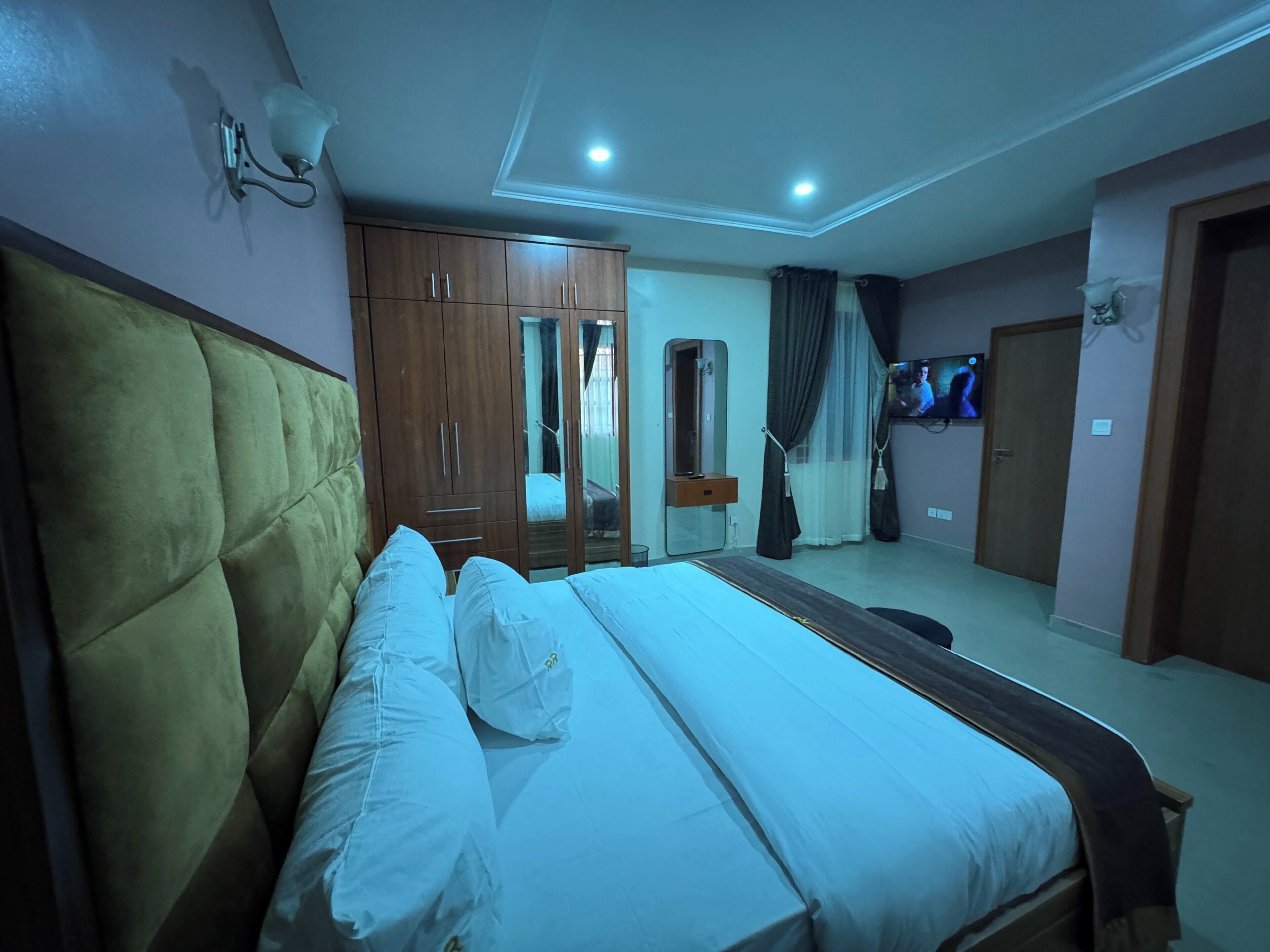 A bedroom with a bed, wardrobe, mirror, TV, and curtains.