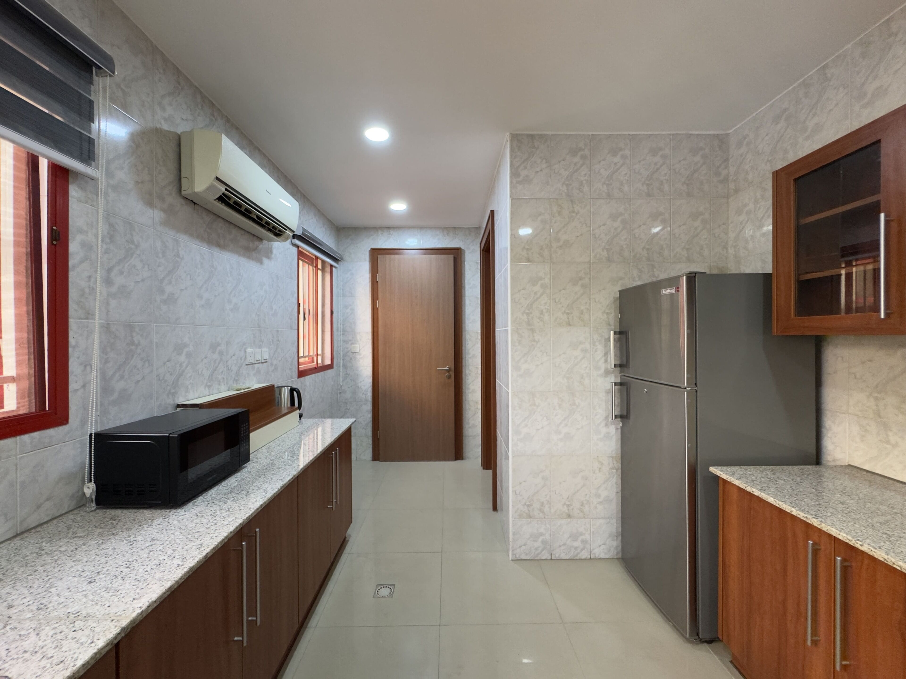 A modern kitchen with marble tiles, a built-in microwave, a stainless steel refrigerator, and wooden cabinets.