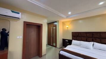 A hotel room with a bed, a wardrobe, a mirror, an air conditioning unit, and a nightstand.