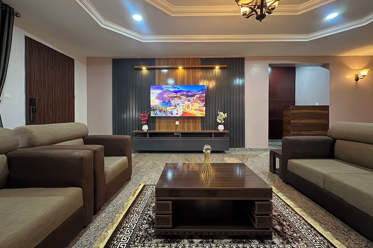 A living room with a flat-screen TV, dark wood paneling, a chandelier, and two sofas.