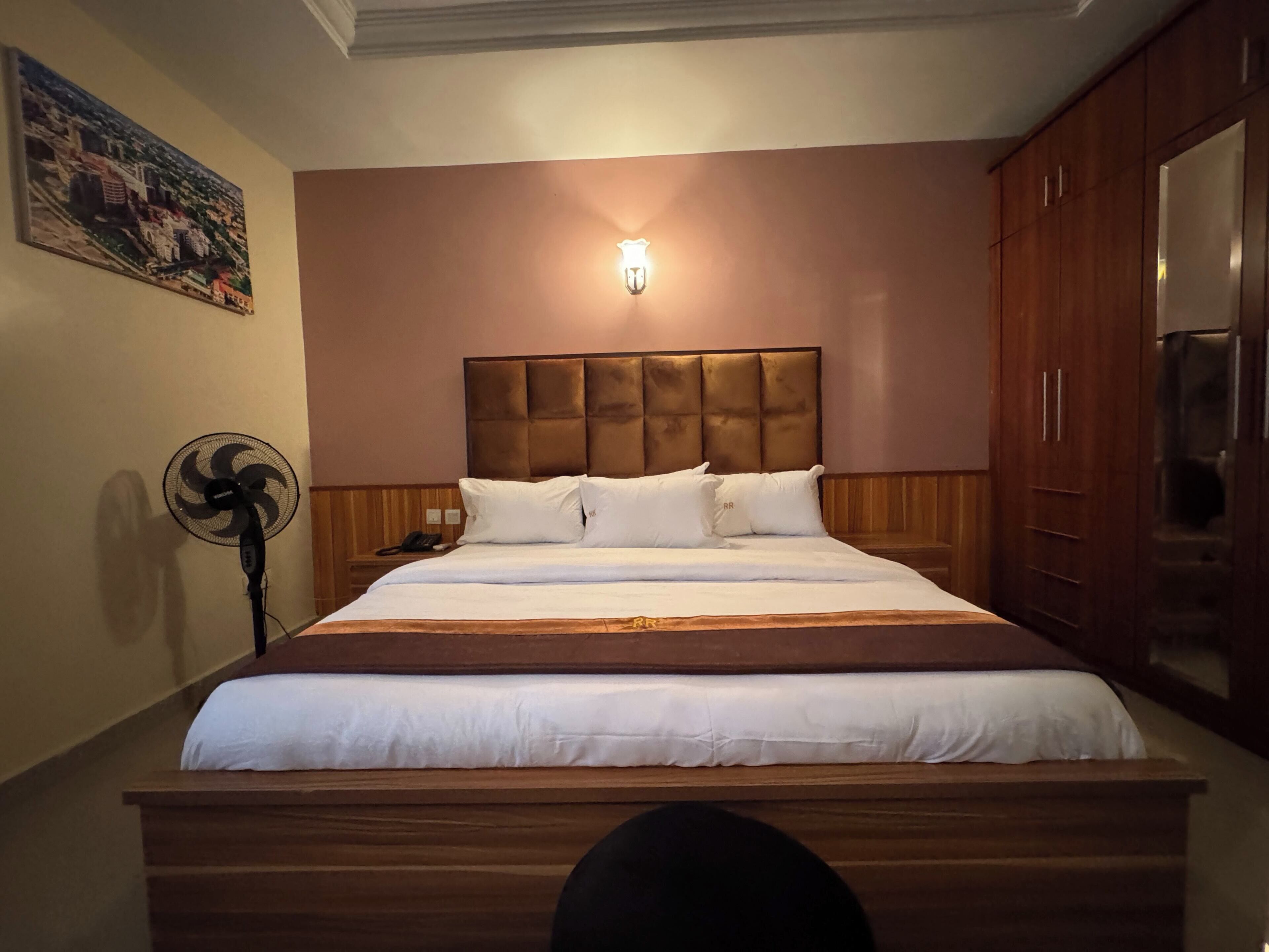 Une chambre d’hôtel avec un grand lit, une table de chevet avec une lampe, un luminaire fixé au mur et un tableau accroché au mur.