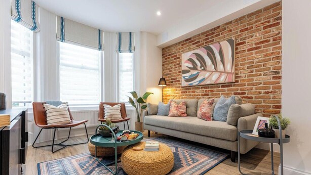 A living room with a brick wall, a sofa, a coffee table, a chair, and a lamp. - St Swithuns Abode - Moments from the train station & beaches (Bournemouth, Christchurch and Poole)