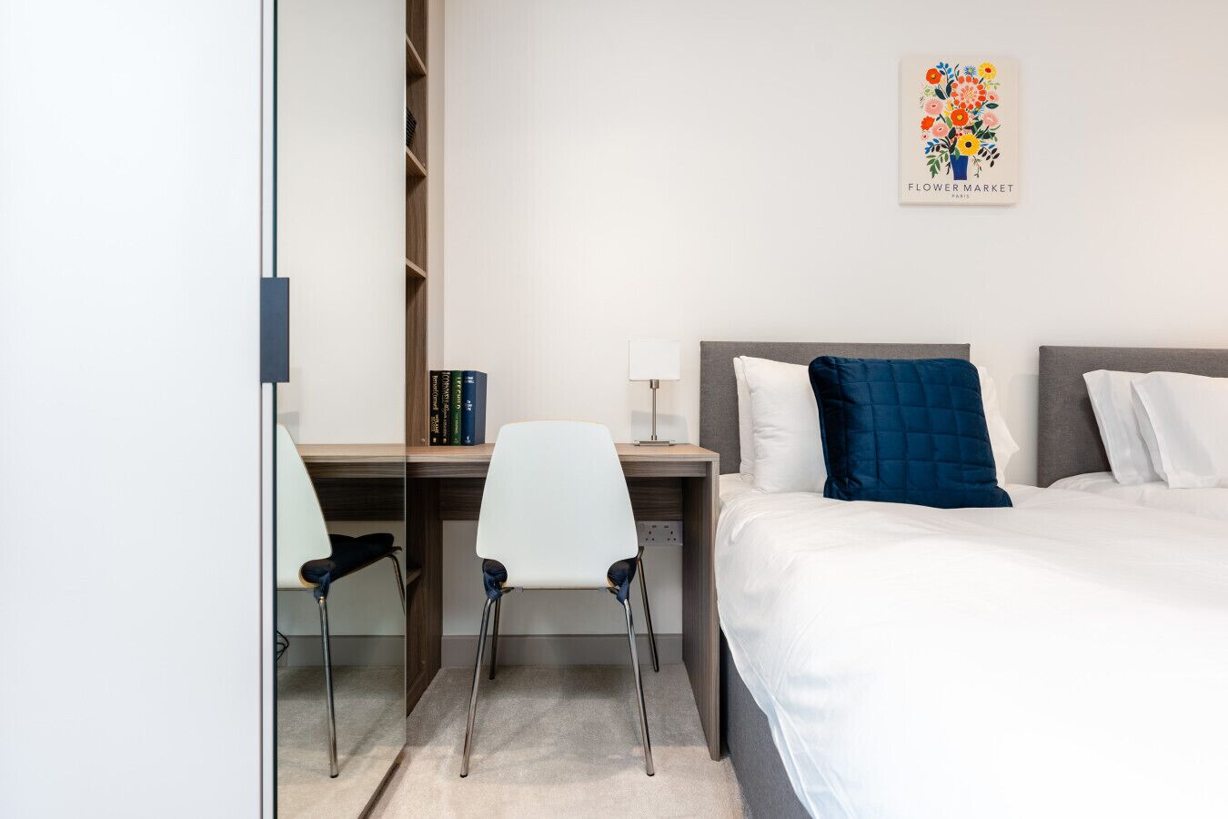 Une chambre d’hôtel comprenant un lit, un bureau avec une chaise, une bibliothèque et une œuvre d’art accrochée au mur.