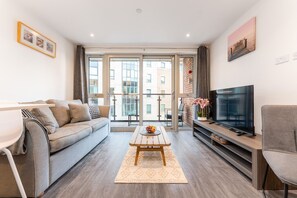 Een moderne woonkamer met een bank, salontafel, televisie en een balkon met glazen deuren.