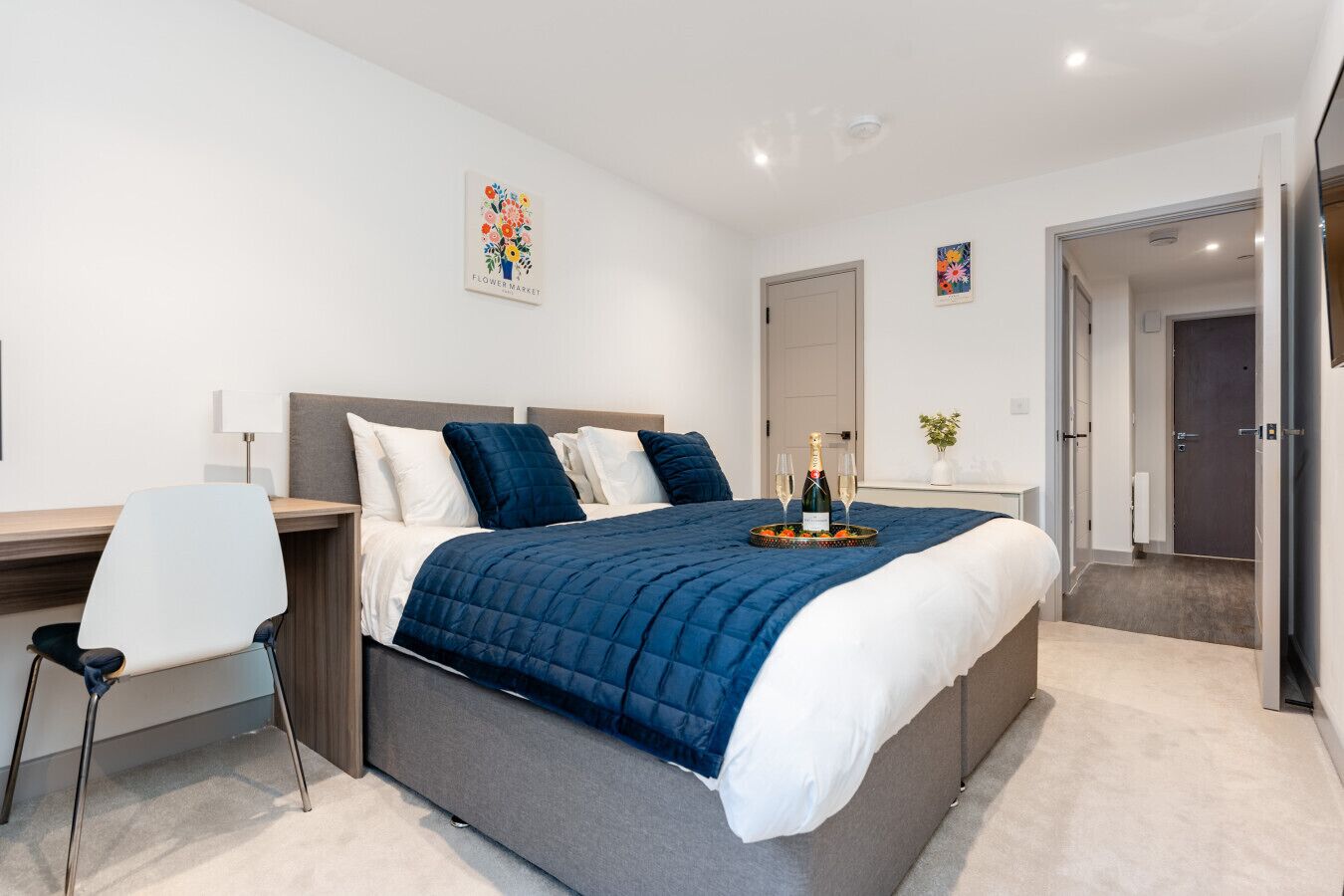 Ein modernes Schlafzimmer mit Bett, Nachttisch, Sessel und einer dekorativen Wandgestaltung.