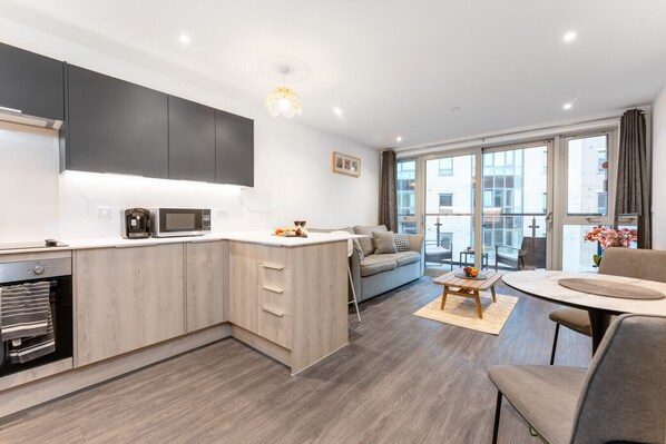 Een moderne keuken met een ingebouwde magnetron, een eethoek met een ronde tafel en een bank.
