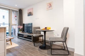 Een moderne woonkamer met een flatscreen televisie, twee grijze fauteuils, een klein rond tafeltje en een houten salontafel.