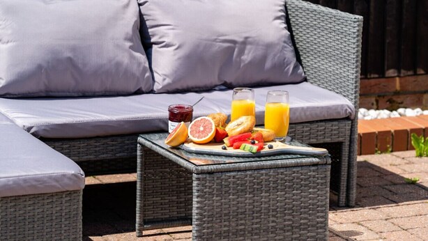 A wicker outdoor seating area with a table set with fruits, a bottle of jam, and glasses of orange juice. - Leaside House - Good access links across Southampton & New Forest (Southampton)