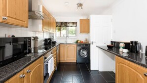 A modern kitchen with wooden cabinets, a built-in washing machine, and a black countertop. - Leaside House - Good access links across Southampton & New Forest (Southampton)