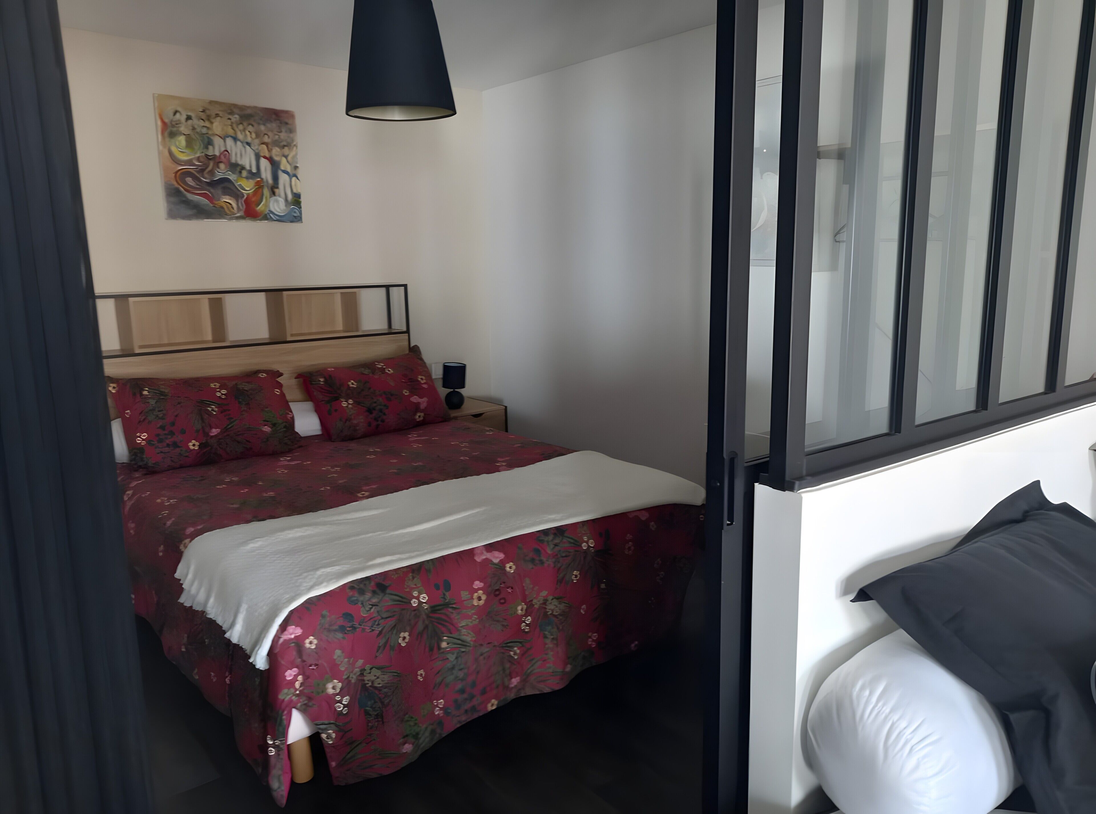 A bedroom with a bed, a nightstand, a lamp, a painting on the wall, and a window with blinds.