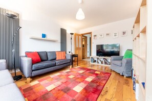 Un salon moderne avec un canapé gris, un téléviseur, un tapis coloré et un plancher en bois.