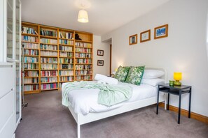 Une chambre à coucher avec un lit blanc, une bibliothèque, une table de chevet et une lampe.