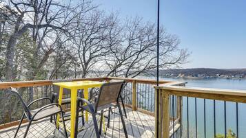 A wooden deck with a table and chairs, overlooking a body of water and trees.