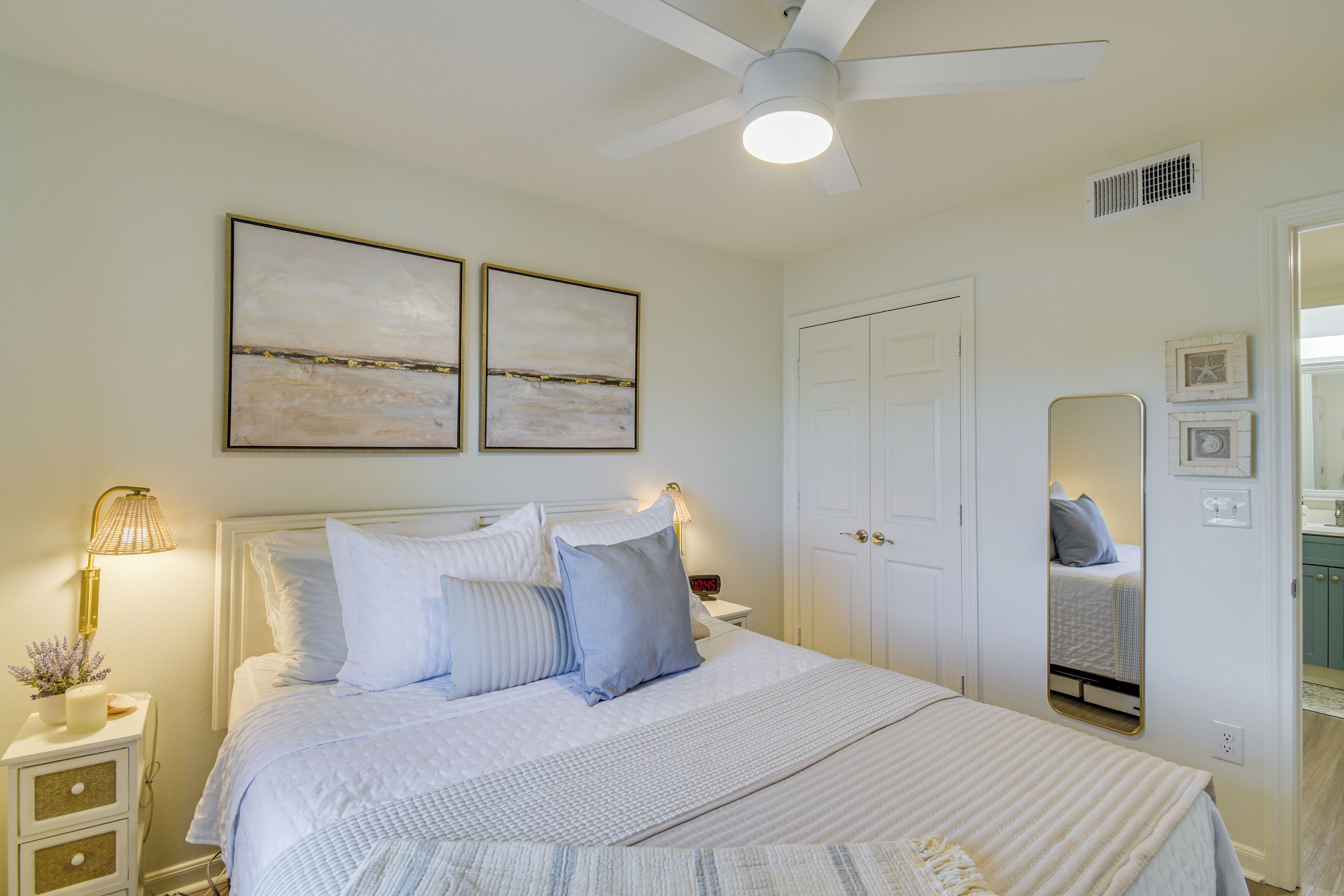 A bedroom with a bed, bedside tables, a ceiling fan, and artwork on the wall.