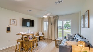 Un salon moderne comprenant un coin repas, un ventilateur de plafond, un téléviseur à écran plat et une grande fenêtre avec des rideaux.