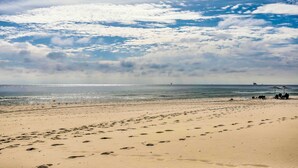 Une plage parsemée d’empreintes, une jetée lointaine et un ciel dégagé.