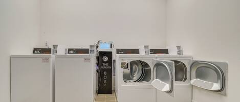 Une buanderie équipée de quatre machines à laver et de quatre sèche-linge, d’un panneau de commande et d’une pancarte sur laquelle on peut lire : « Le maître de la buanderie ».