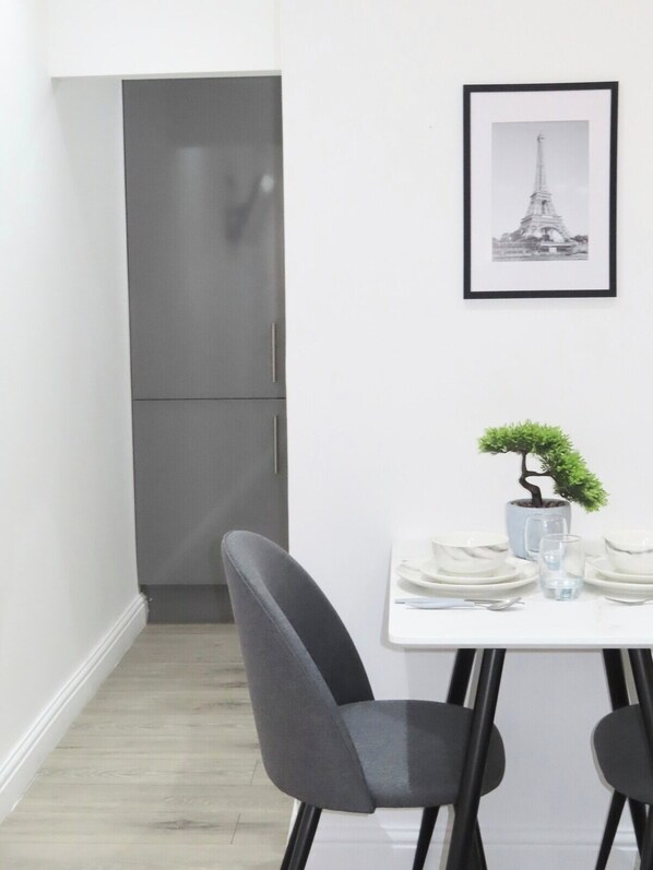 A modern dining area with a white table, grey chairs, a small potted plant, and a framed picture of a tower.
