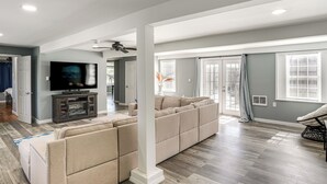 Un salon moderne avec un canapé d’angle, un téléviseur à écran plat et un ventilateur de plafond.