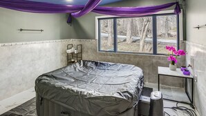 Une salle de bain avec une baignoire, une fenêtre donnant sur les arbres et un vase rempli de fleurs posé sur une petite table.