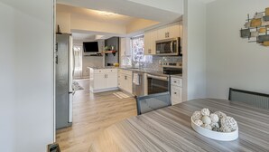 A modern kitchen with white cabinets, a built-in microwave, and a dining area with a wooden table and decorative bowls. - Renovated Townhome w/ Garage, 12 Mi to St Louis (Belleville)