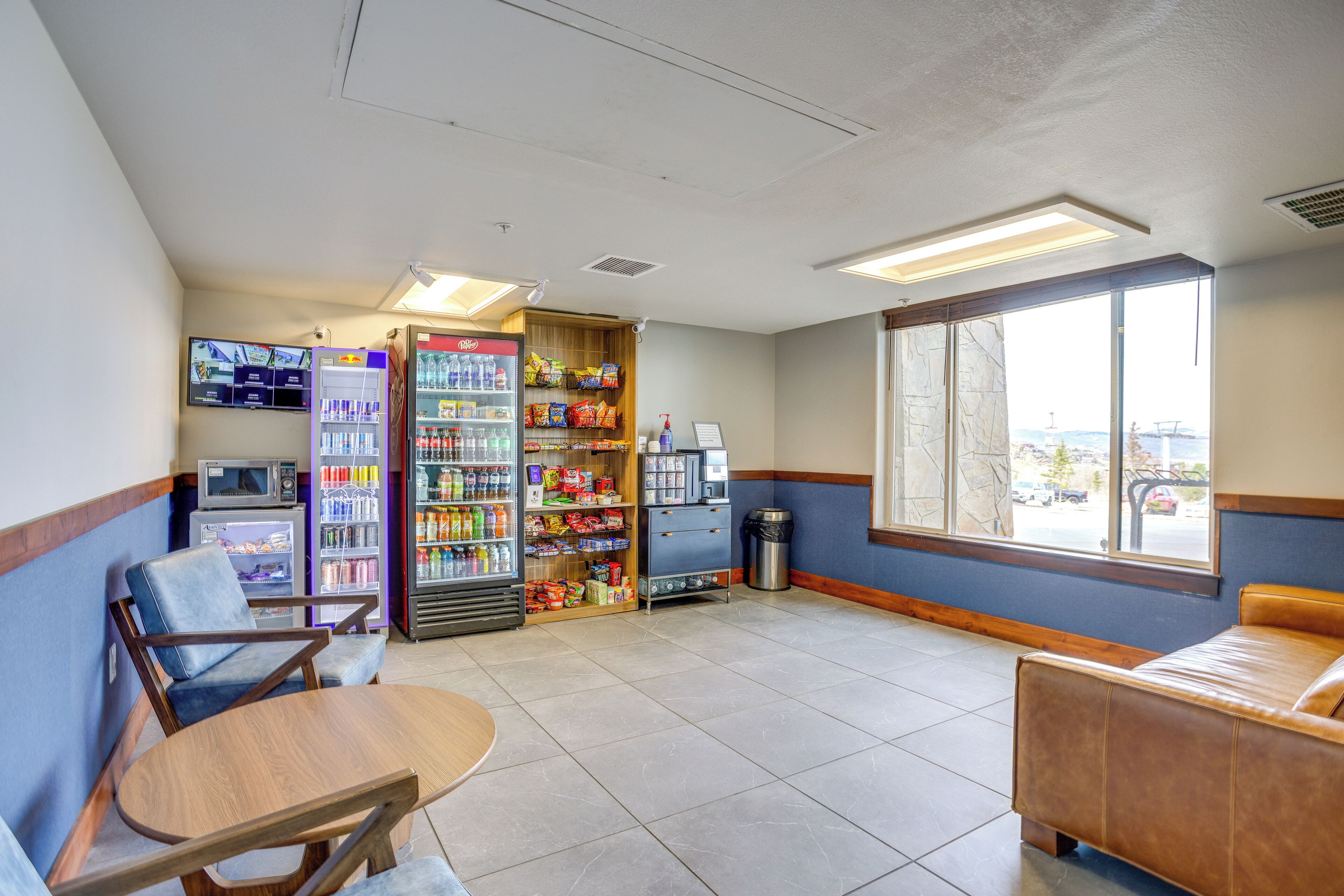 A room with a seating area, a vending machine, a trash can, and a window with a view.