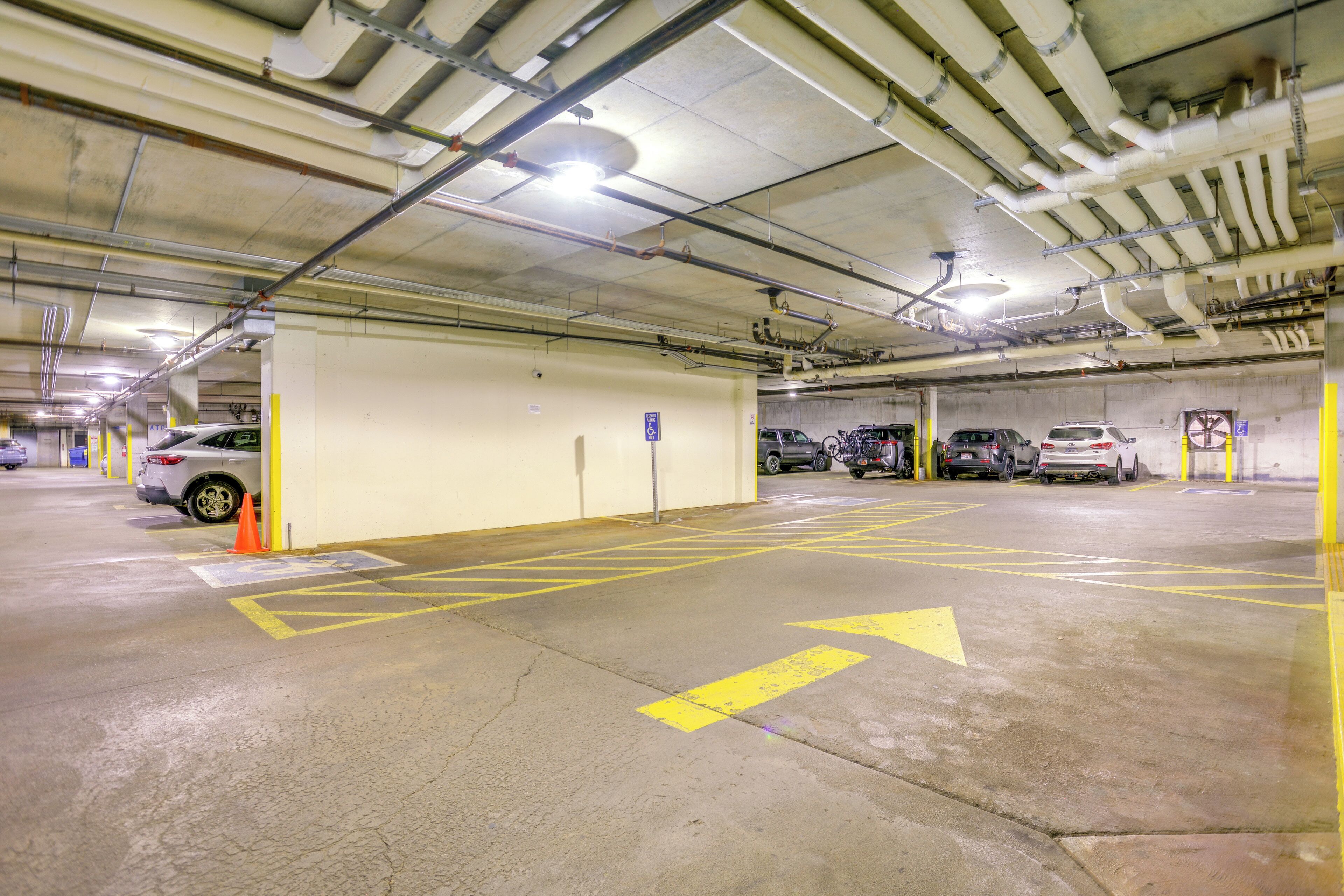 Eine mehrstöckige Parkgarage mit Betonböden, gelben Pfeilen zur Orientierung und mehreren parkenden Autos.