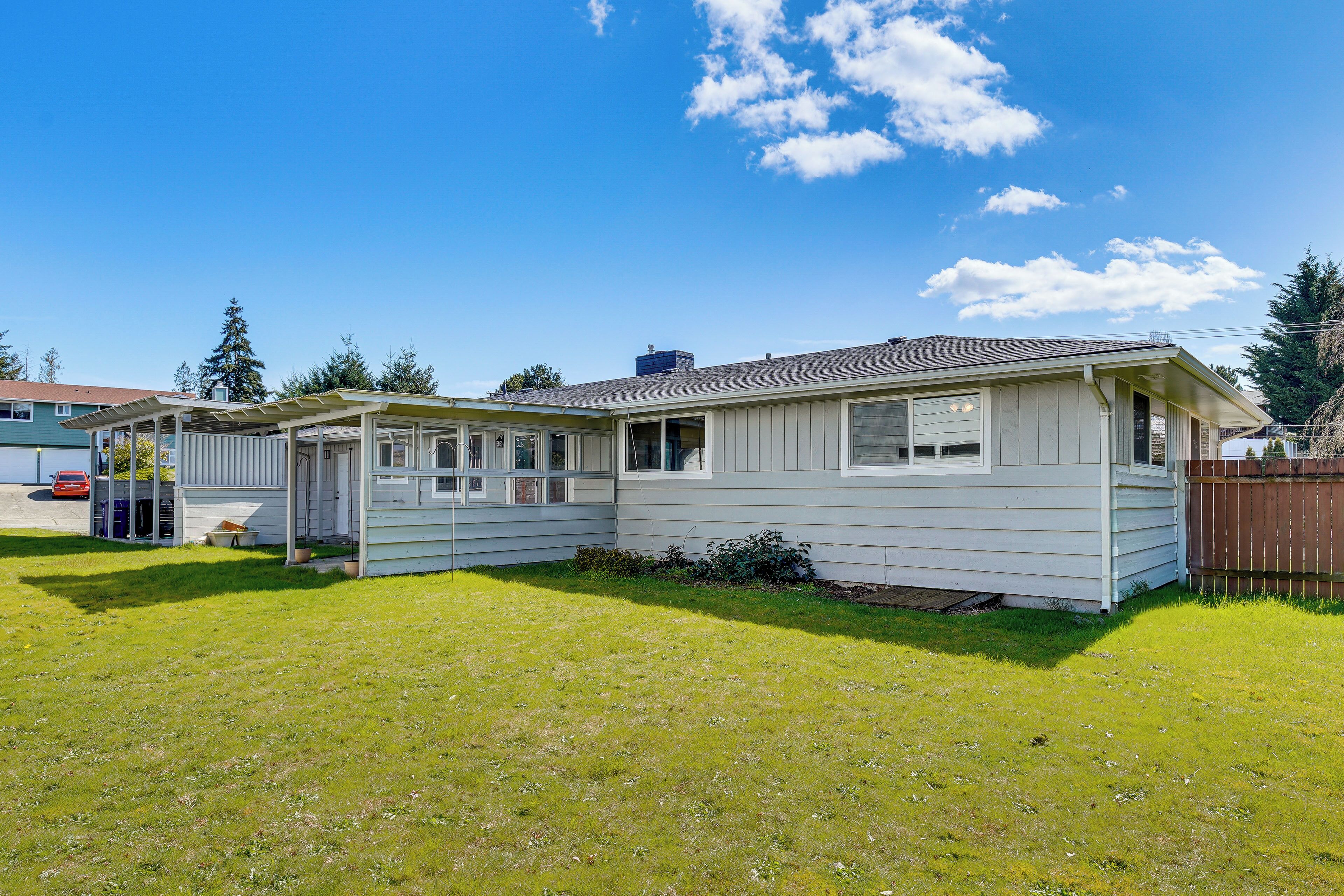 A single-story house with a covered porch, a fenced yard, and a clear blue sky.