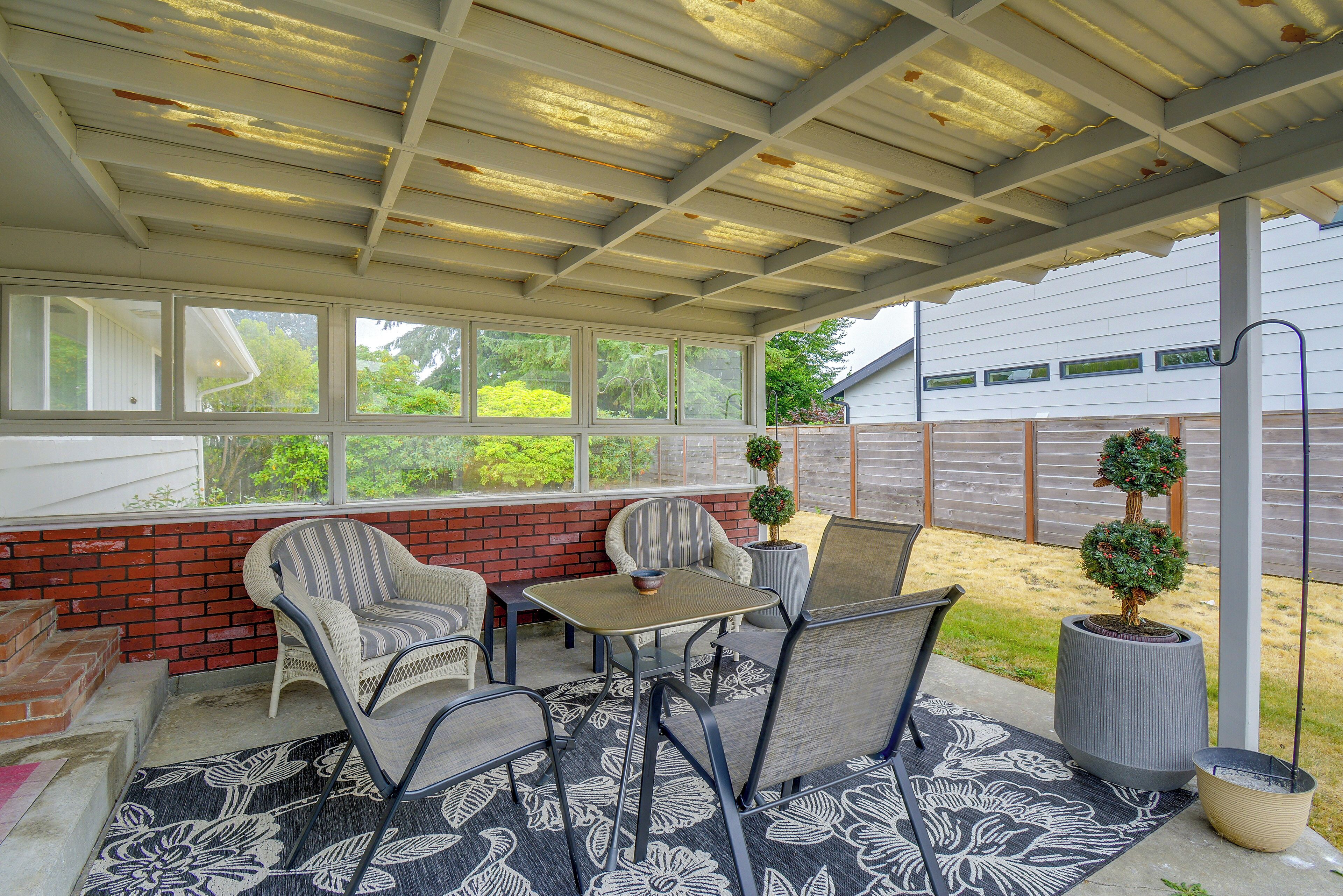 Eine überdachte Terrasse mit Tisch und Stühlen, eine Ziegelwand und Blick auf einen Garten.