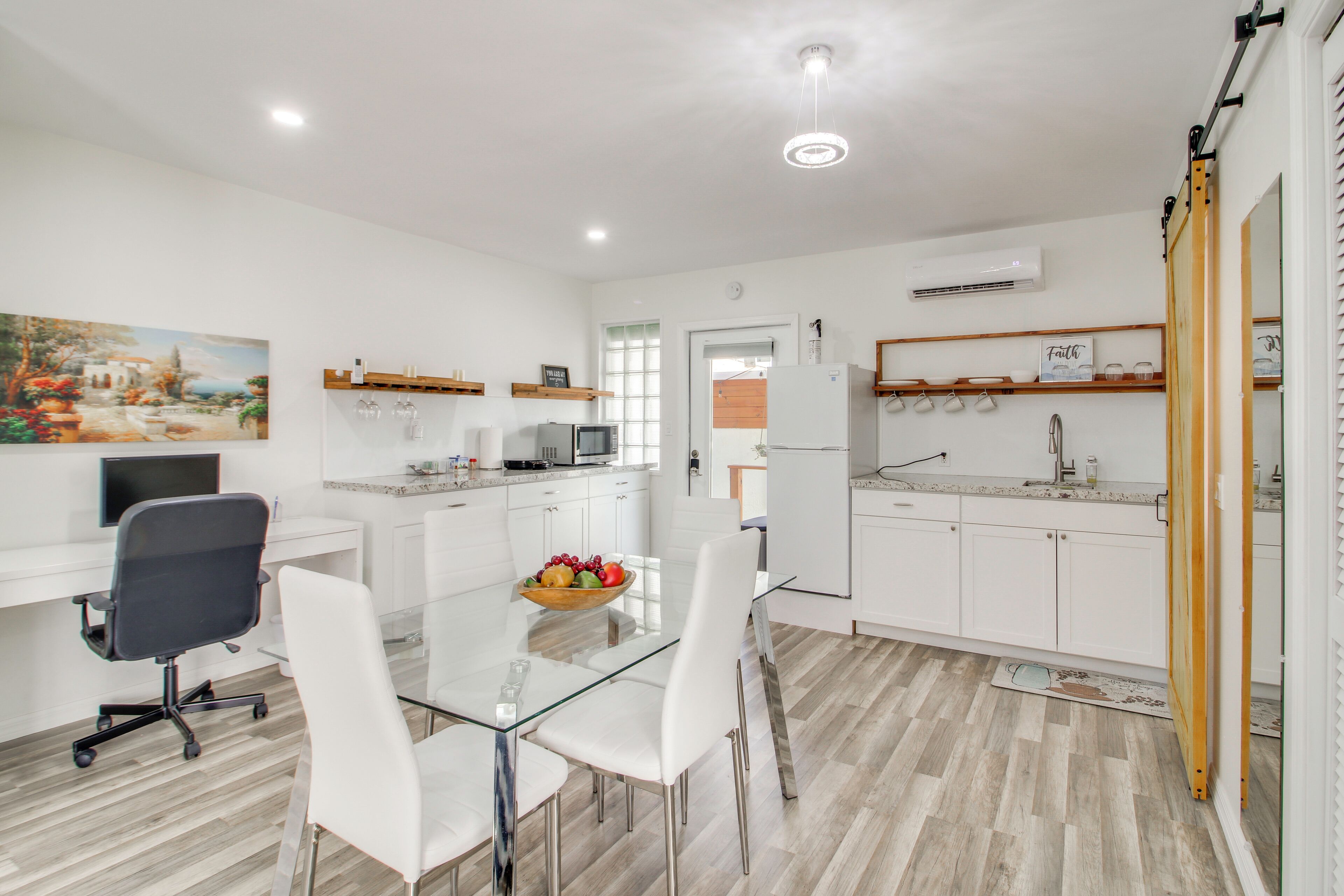 A modern kitchen with white cabinets, a glass dining table, and a fruit bowl.